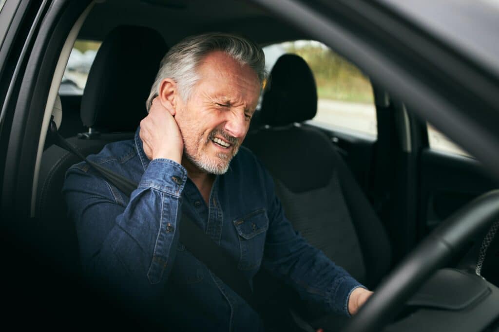 Conductor masculino mayor dentro del automóvil después de un accidente de tráfico que sufre de lesiones por latigazo cervical